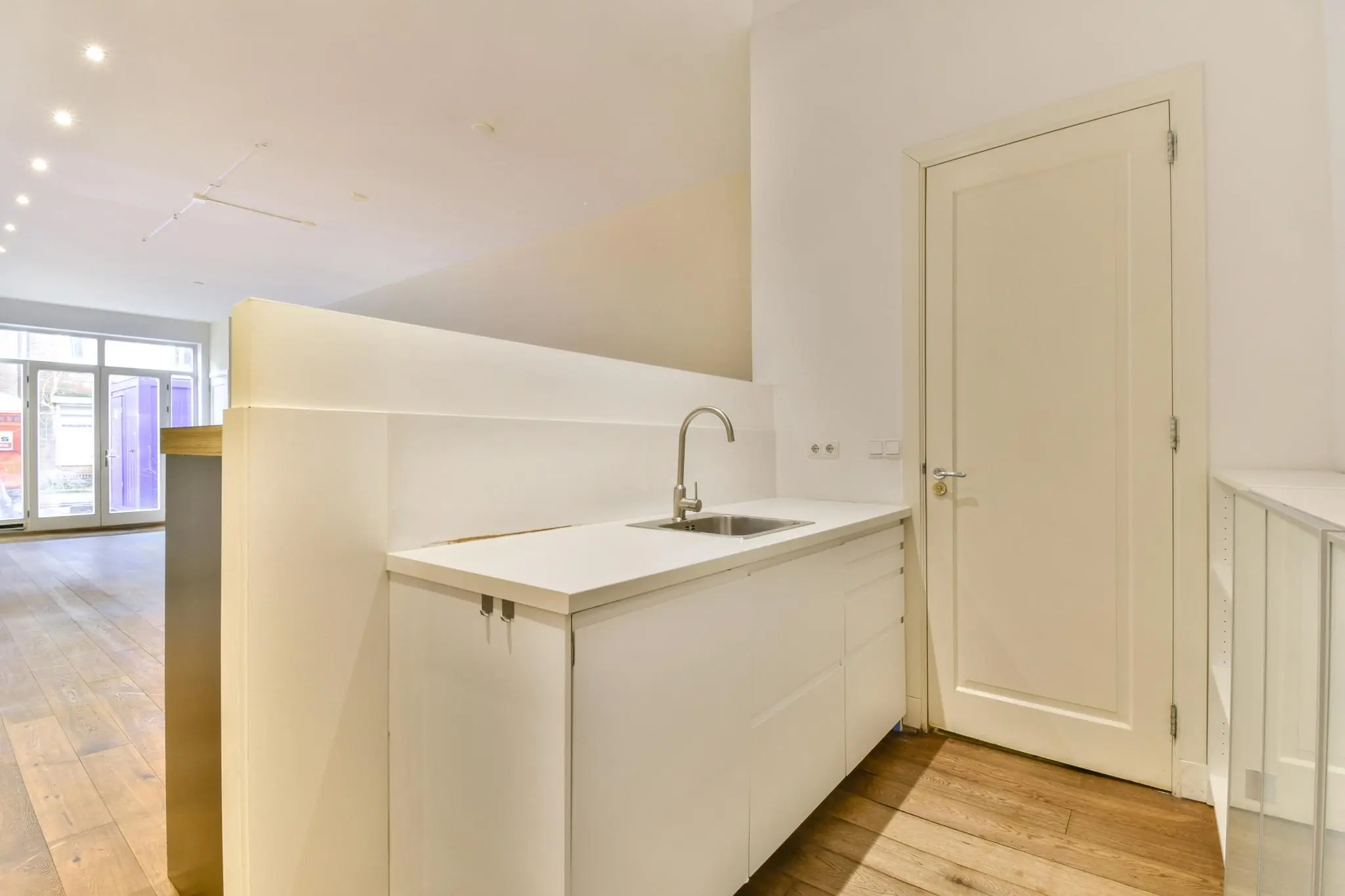 Moderne, lichte keuken met witte kasten, een ingebouwde spoelbak en houten vloer in een woning aan de Korte Schimmelstraat.